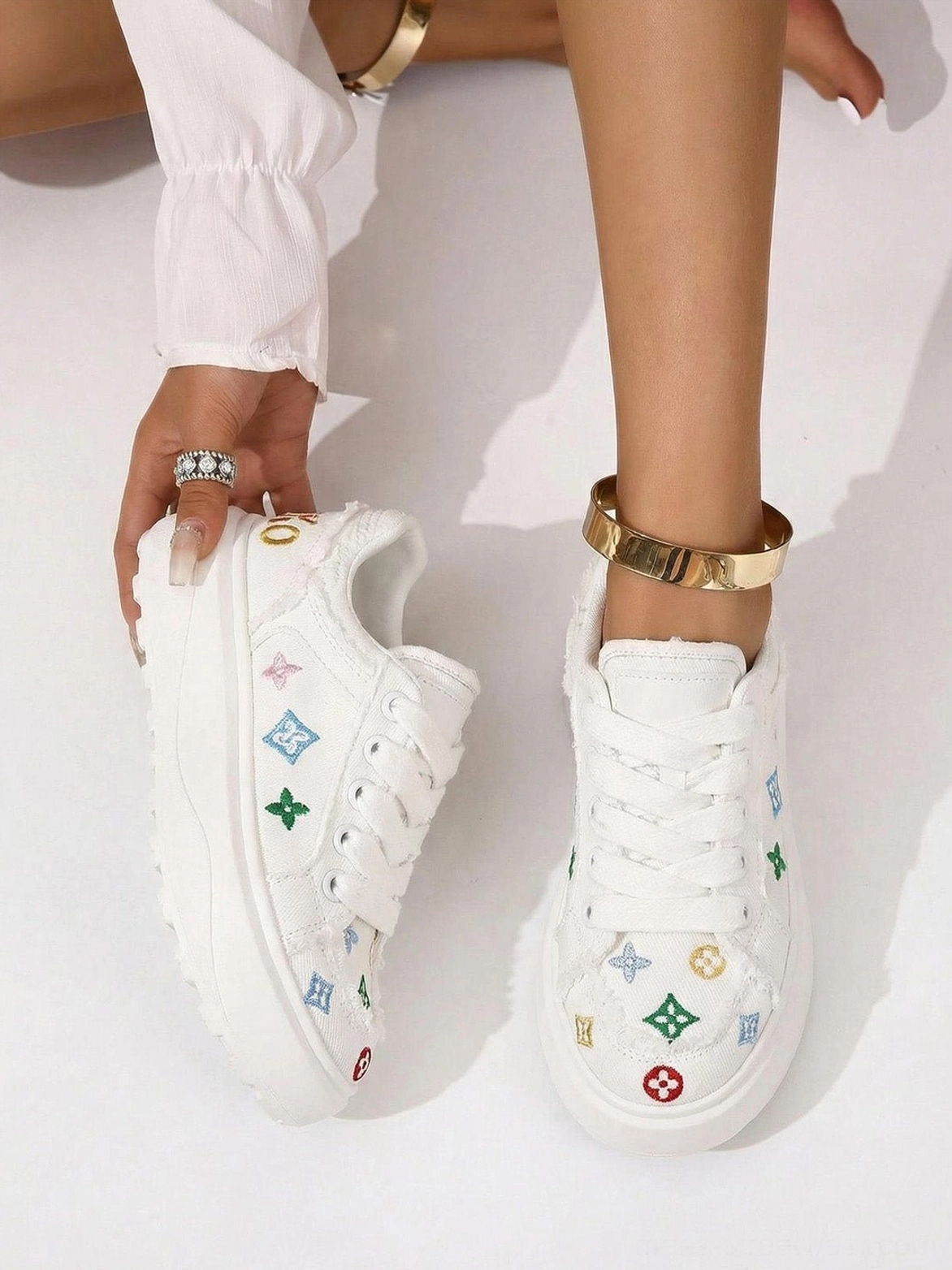Overhead view of white platform skate sneakers with colorful embroidered accents classic laces chunky outsole and gold accessories in a modern streetwear styling scene