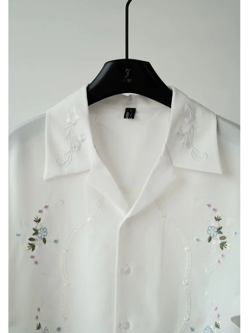Close-up view of a white embroidered camp collar shirt showing delicate floral details and button front