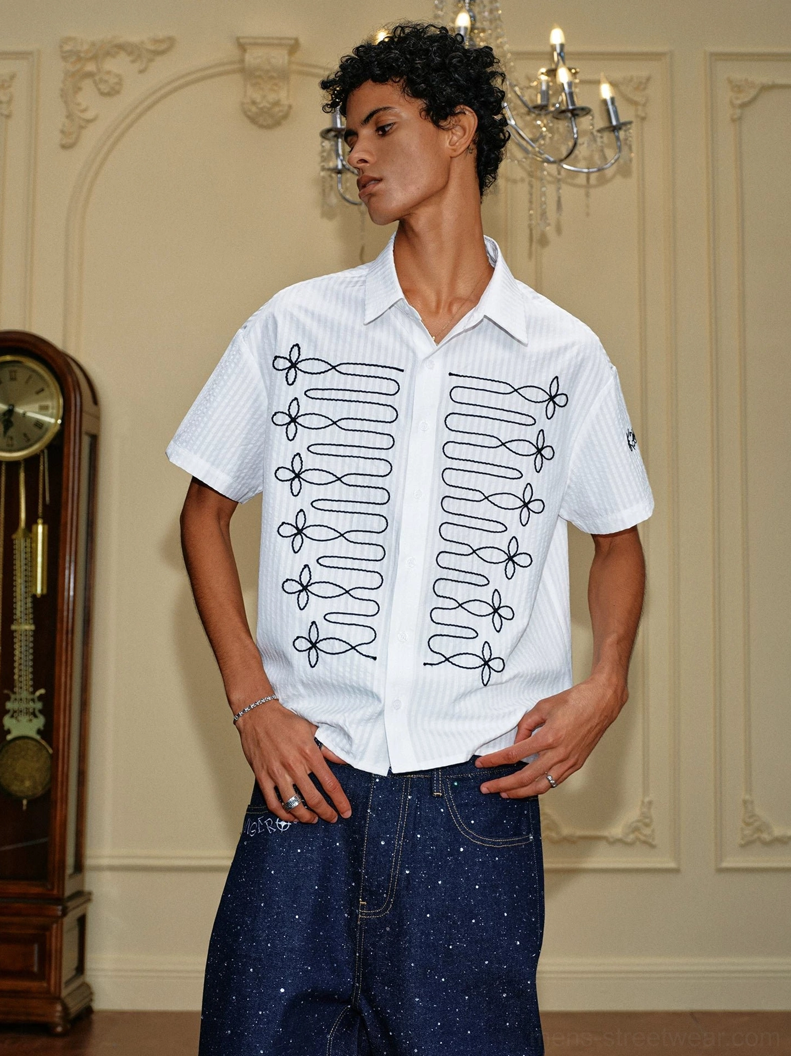 Three-quarter view of white embroidered loop shirt with black front embroidery styled with dark starry denim jeans