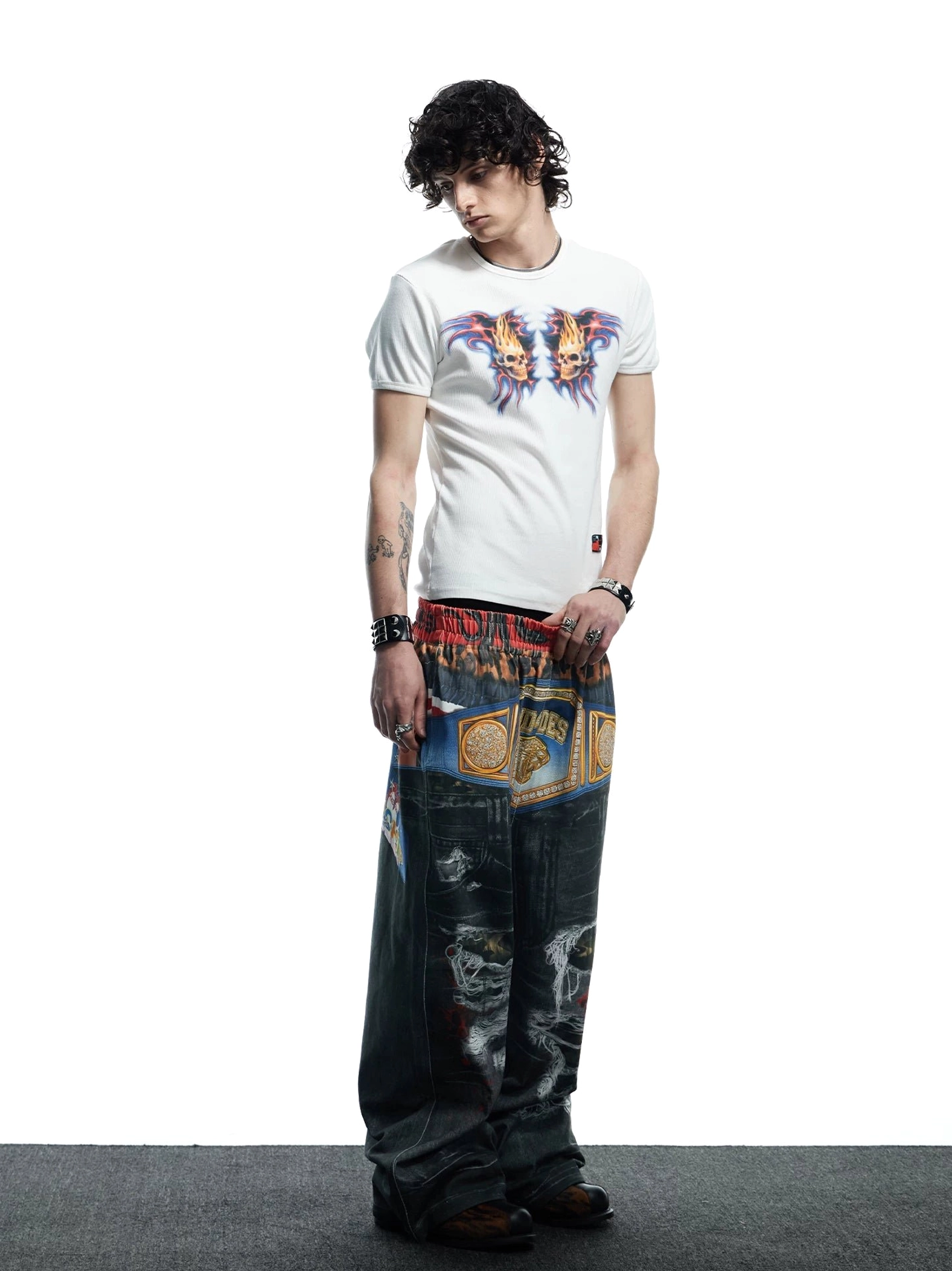 Side front view of fitted white flaming skull tee paired with customized wide-leg denim and statement streetwear belt graphics