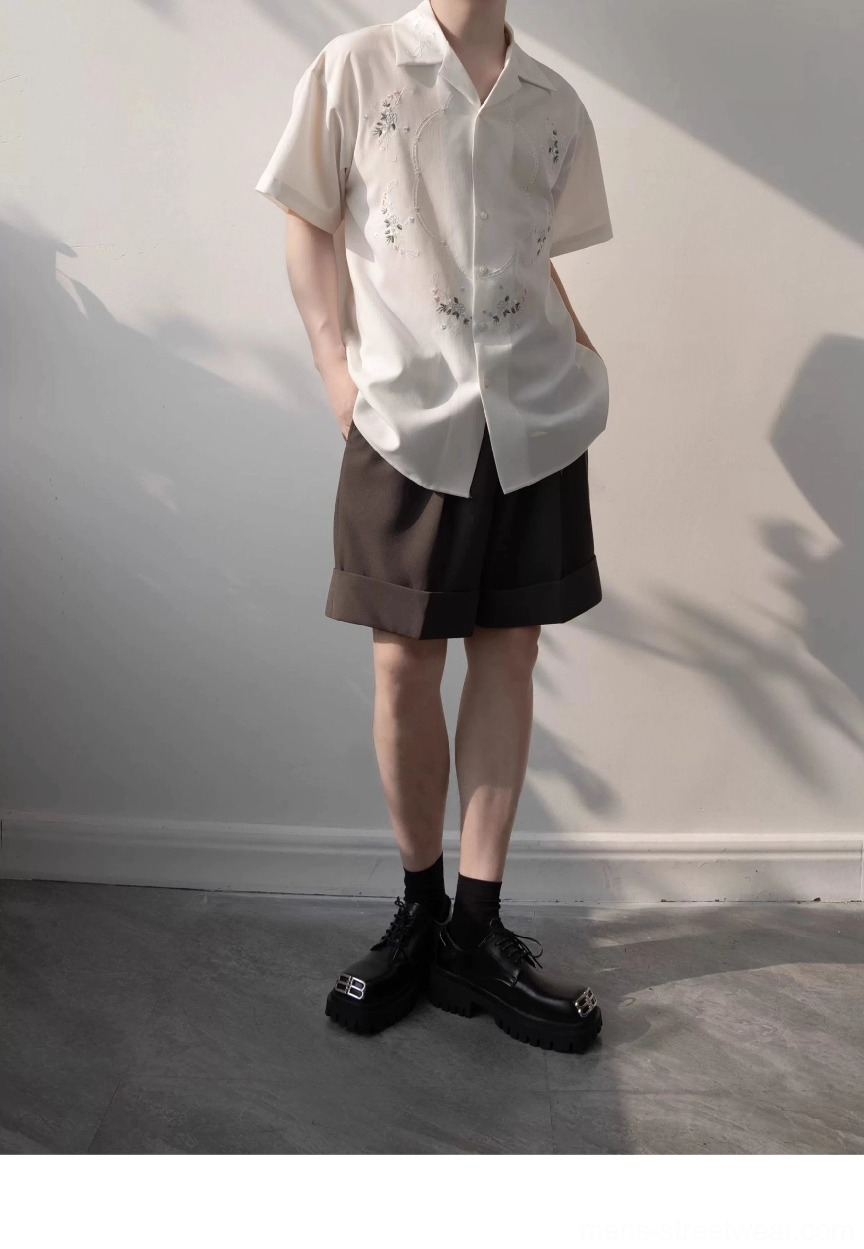 Full body streetwear outfit featuring a white floral embroidered camp shirt, black crew socks, brown shorts, and chunky loafers