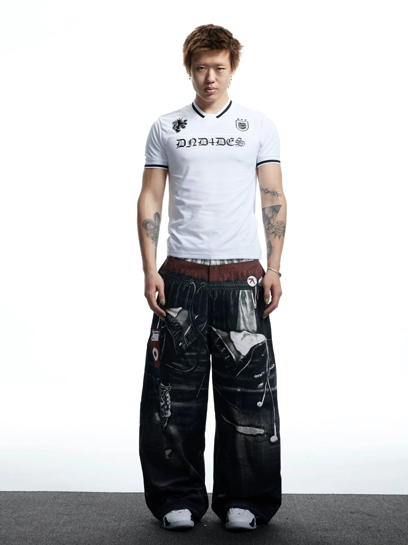 Full front outfit view featuring a white football jersey mesh T-shirt styled with graphic wide-leg denim pants and white sneakers