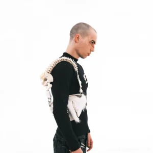 Male model wearing white faux bone spine handle shoulder bag with fur accents in minimalist studio