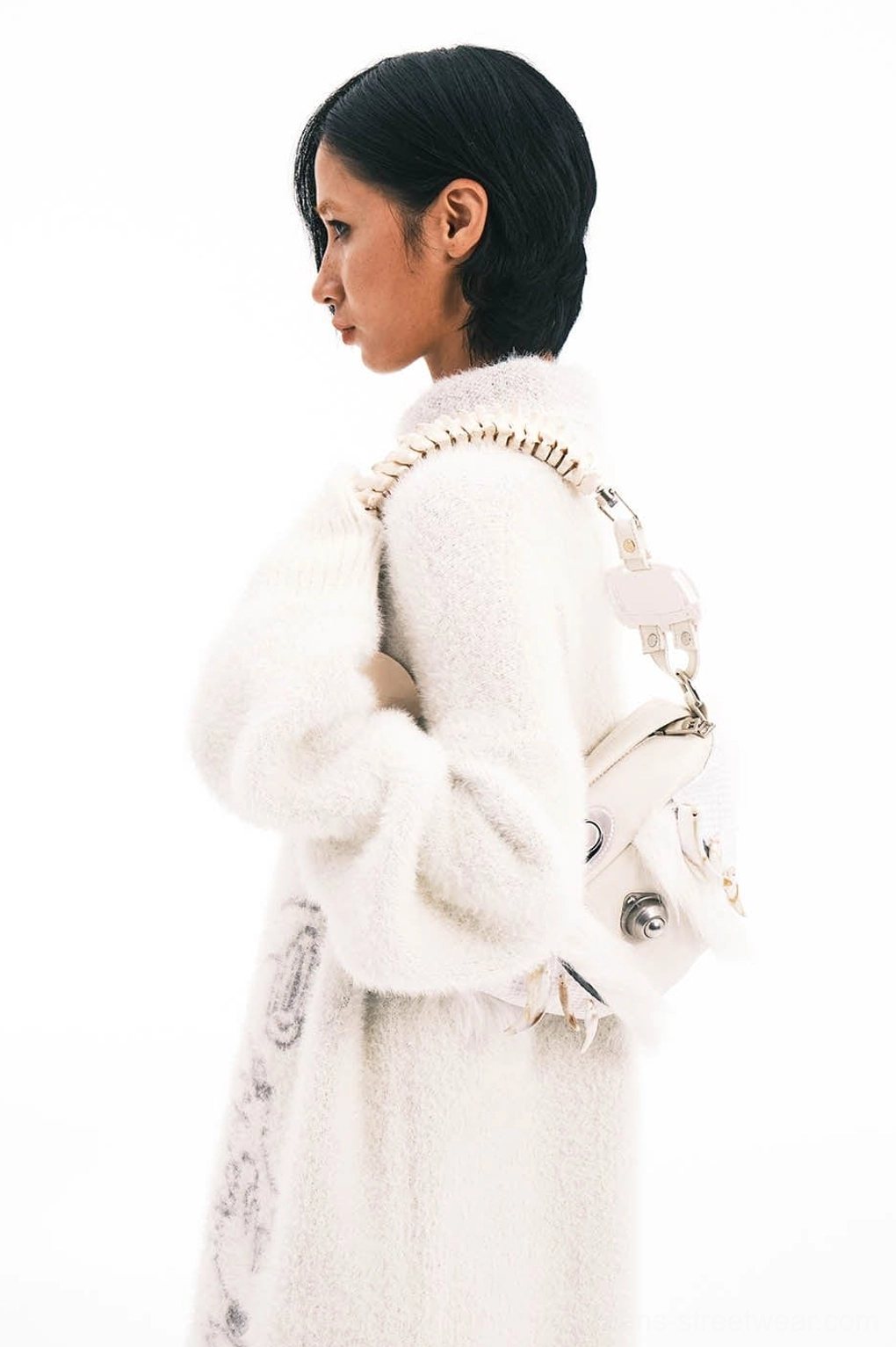 Female model wearing white fur accented shoulder bag with sleek faux bone spine strap in white studio