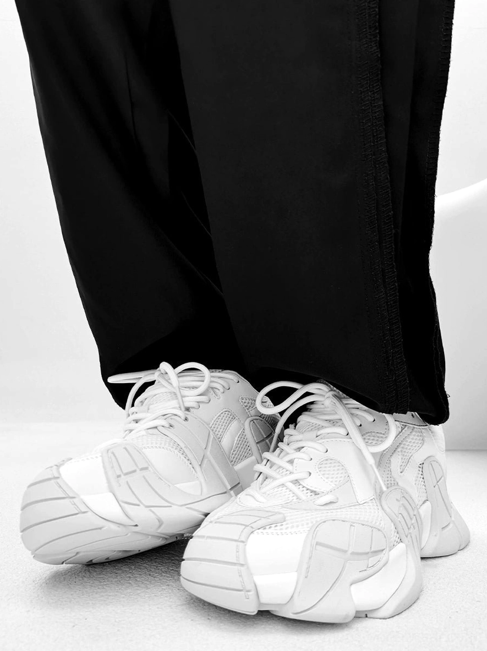 Pure white futuristic chunky platform sneakers worn with wide-leg black streetwear trousers, round toe, lace-up design, and elevated sole