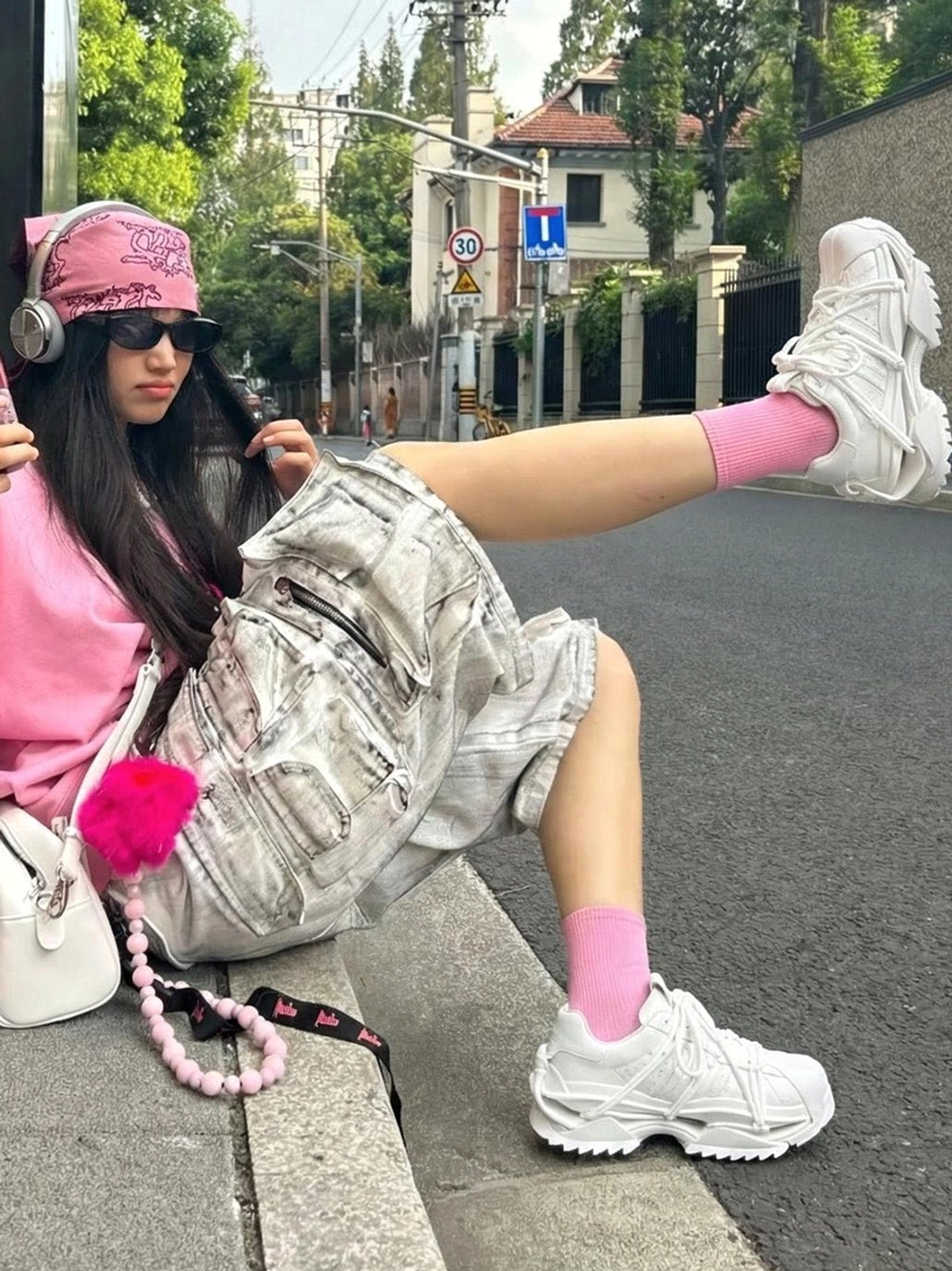 White futuristic chunky sneakers worn with pink socks and casual accessories in an outdoor urban street-style setting