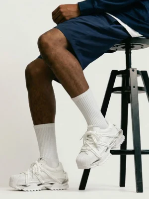 White futuristic runner sneakers worn with navy shorts and white crew socks in a modern casual streetwear outfit