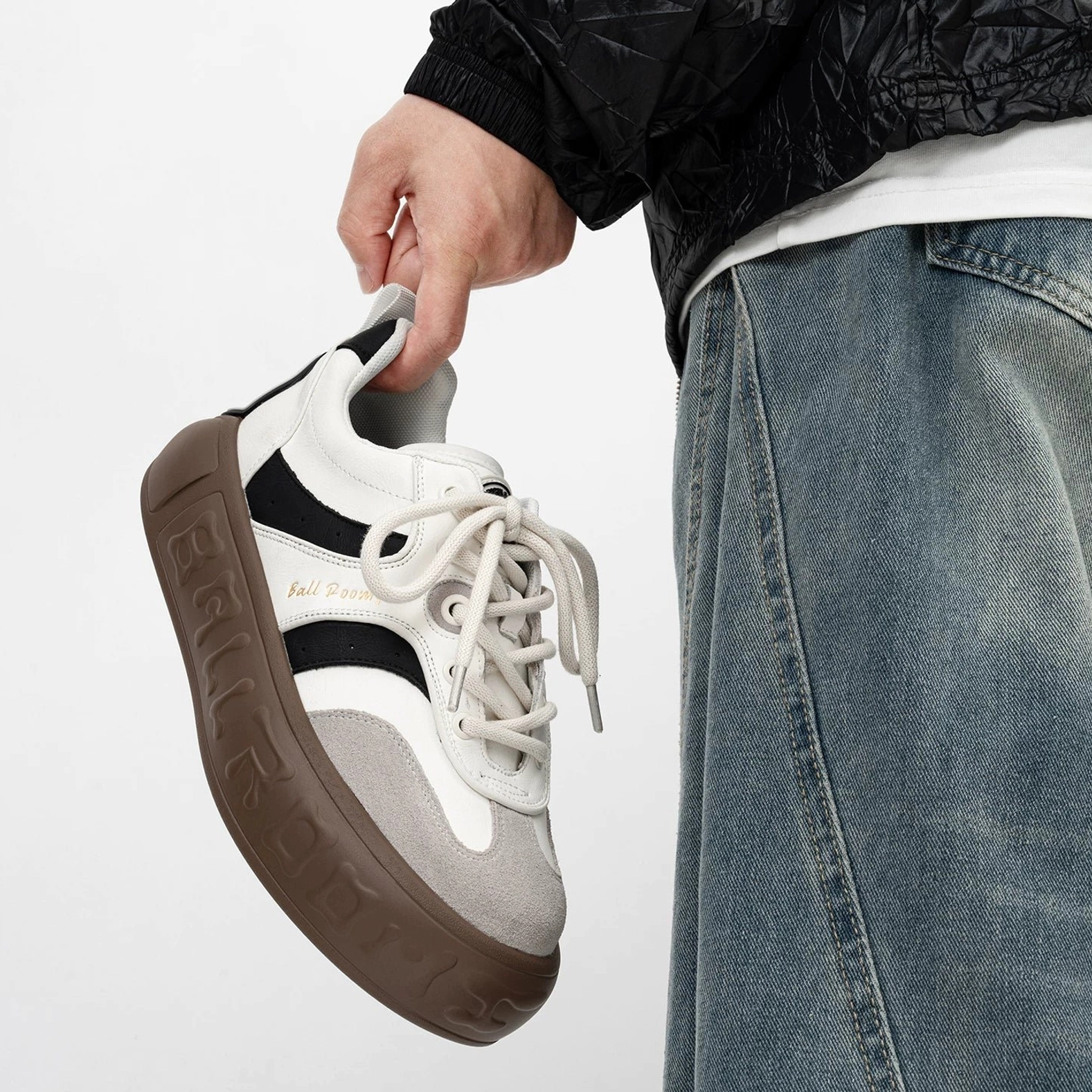 White gray and brown casual skate sneakers with contrast paneling gold tone upper detail and thick embossed gum rubber outsole worn with baggy denim