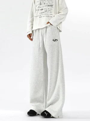 Model wearing white gray logo wide-leg sweatpants with full-length relaxed silhouette, printed long-sleeve top, and black sneakers