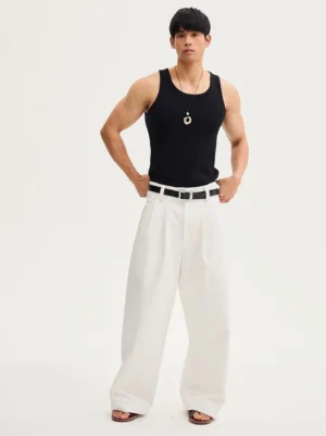 Front view of white high-waisted tailored wide-leg trousers with sharp pleats, black leather belt, black tank top, and leather slides in a minimalist studio