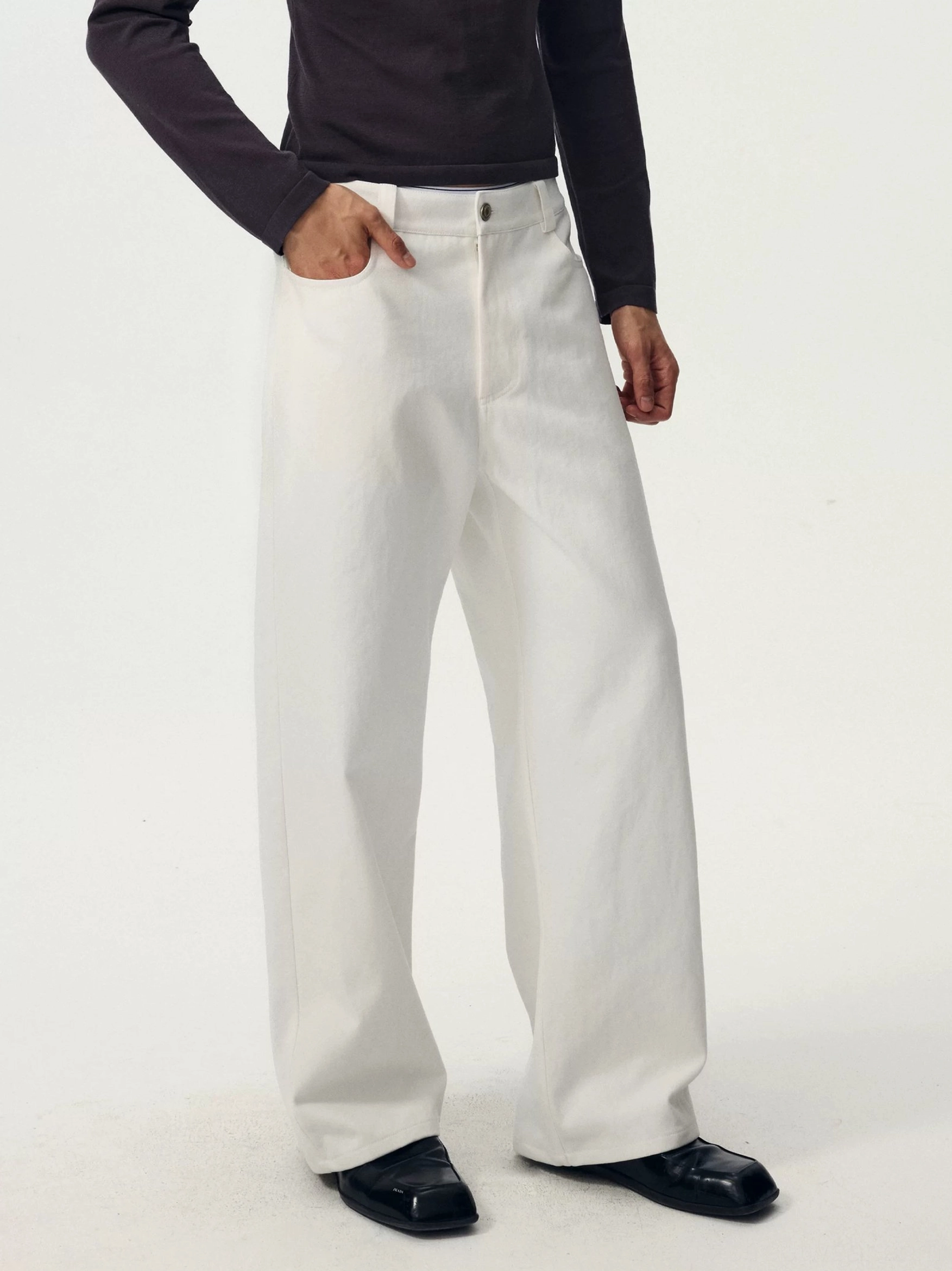 Close lower-body view of white high-waisted wide-leg denim trousers showing the button-fly waist and smooth cotton fabric