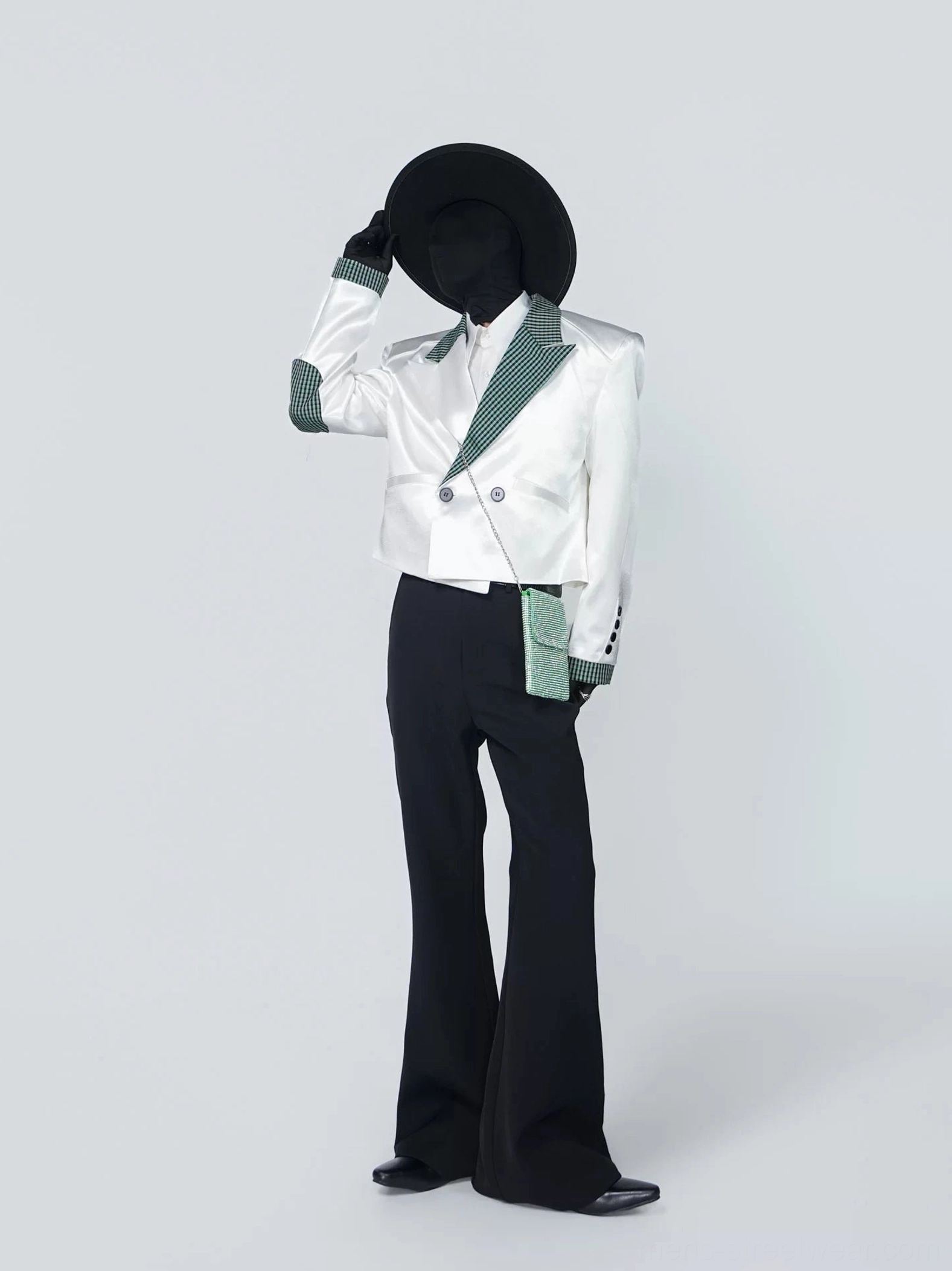 Side three-quarter styling view of a glossy white houndstooth-trim blazer with black flared trousers and matching green accent bag