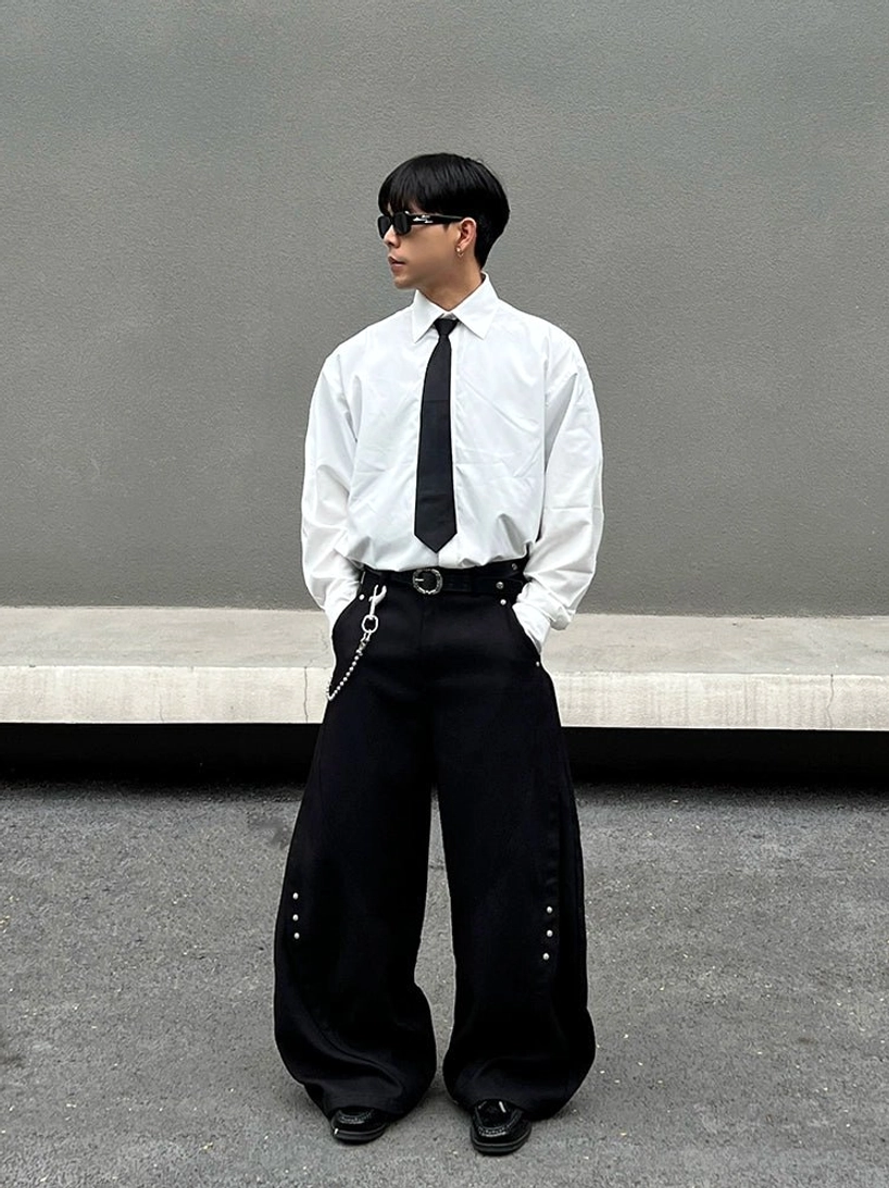 Side view of a white Korean streetwear dress shirt styled with a black tie, sunglasses, wide-leg pants, chain belt, and metal stud accessories