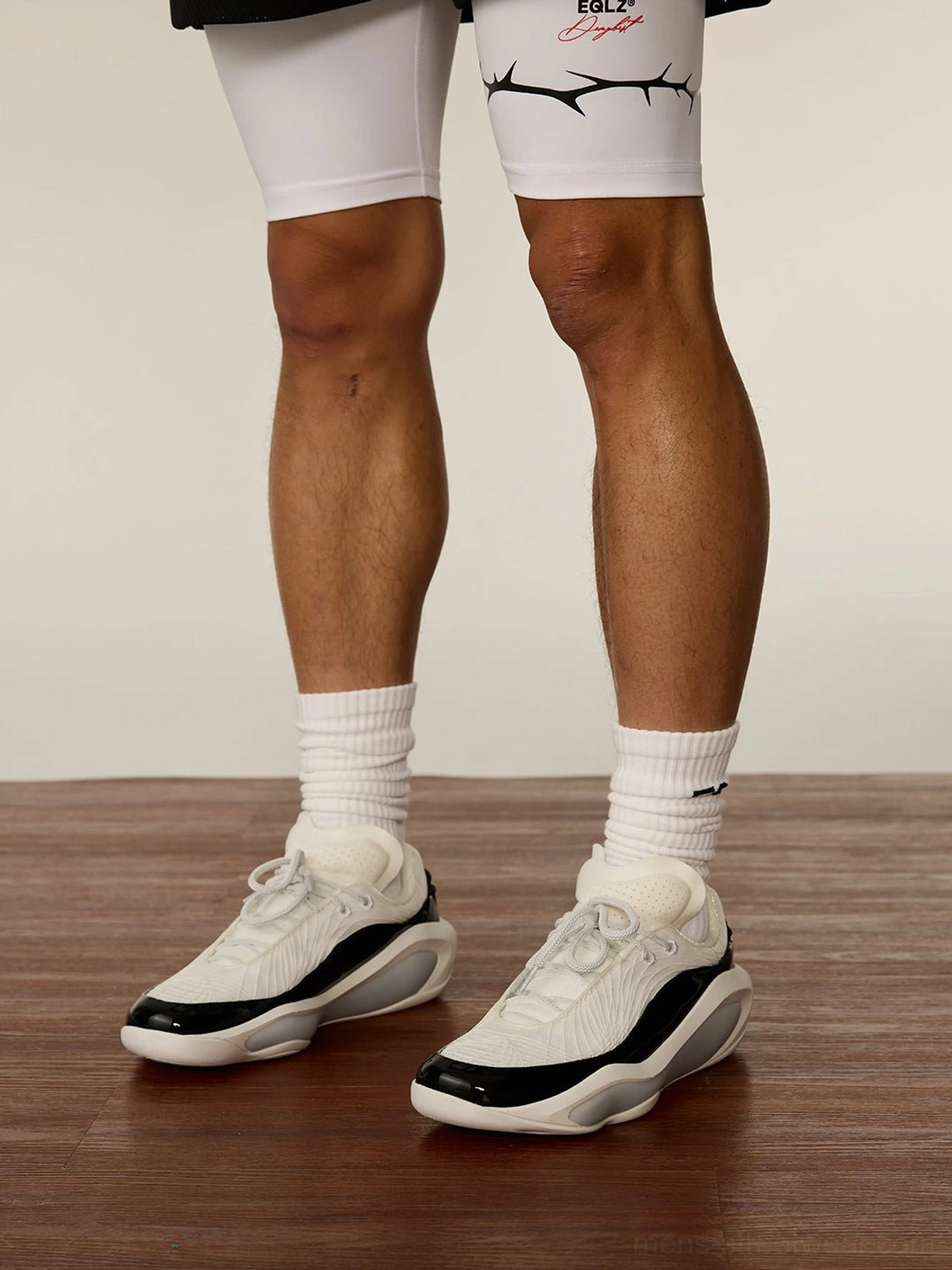 Male model wearing white leather basketball sneakers with crew socks on an indoor wooden court floor