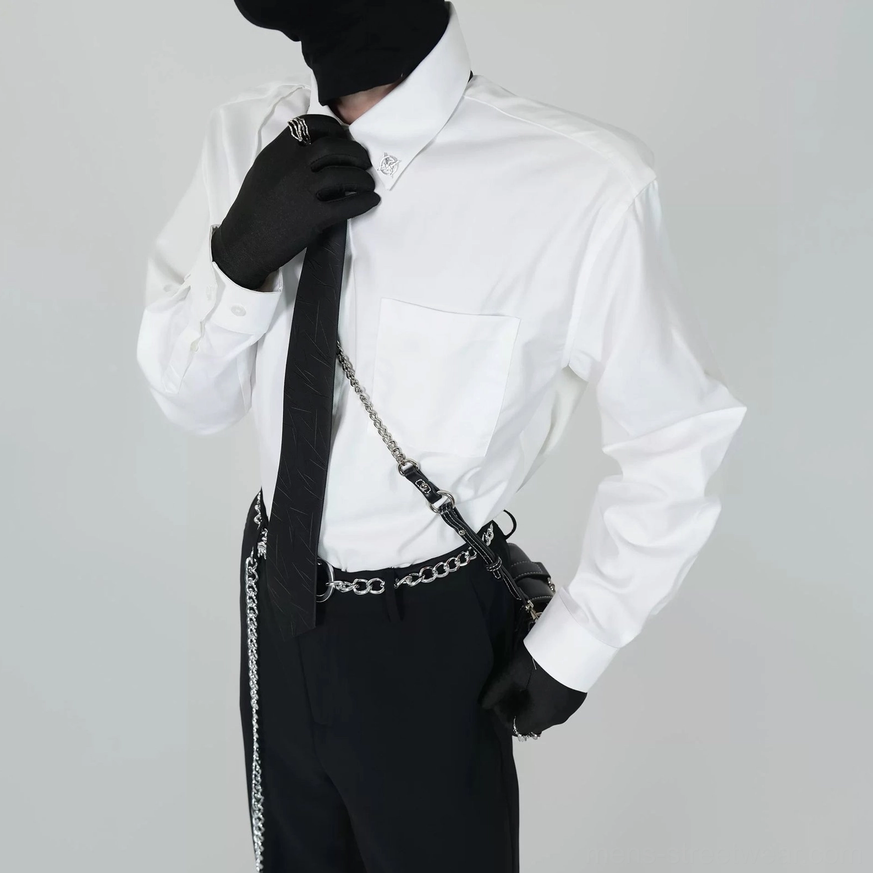 White long sleeve dress shirt with chest pocket and patterned black tie styled with black gloves, chain belt, and crossbody bag