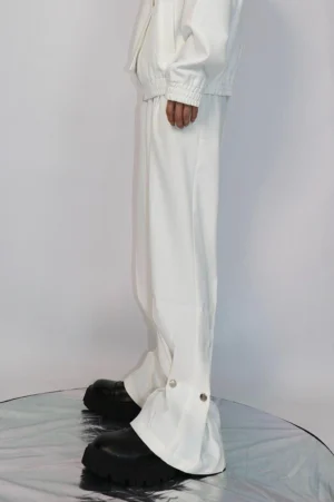 White loose straight streetwear trousers with high waist, relaxed oversized fit, and metal snap cuff details styled with a matching jacket and black platform shoes