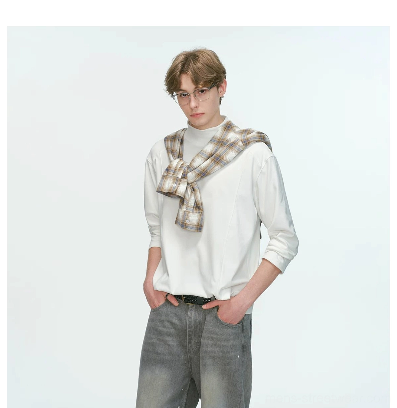 White men's mock neck long sleeve top styled with a plaid shirt over the shoulders, black belt, and gray jeans