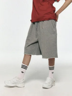 White technical runner sneakers worn with grey sweat shorts and striped crew socks in a casual streetwear outfit