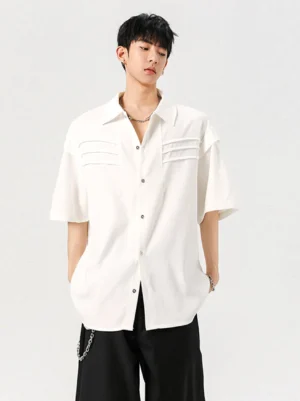 White oversized pleated panel short sleeve streetwear shirt shown from the front with relaxed shoulders and wide-leg black trousers