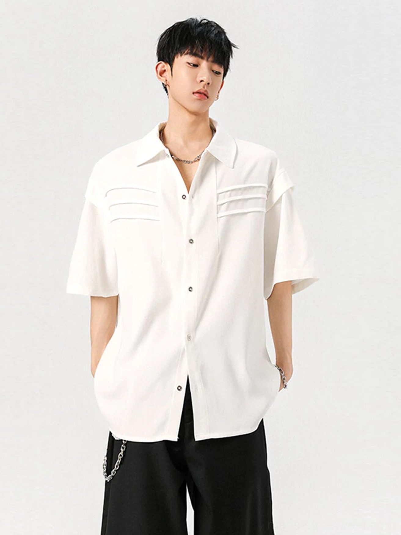 White oversized pleated panel short sleeve streetwear shirt shown from the front with relaxed shoulders and wide-leg black trousers