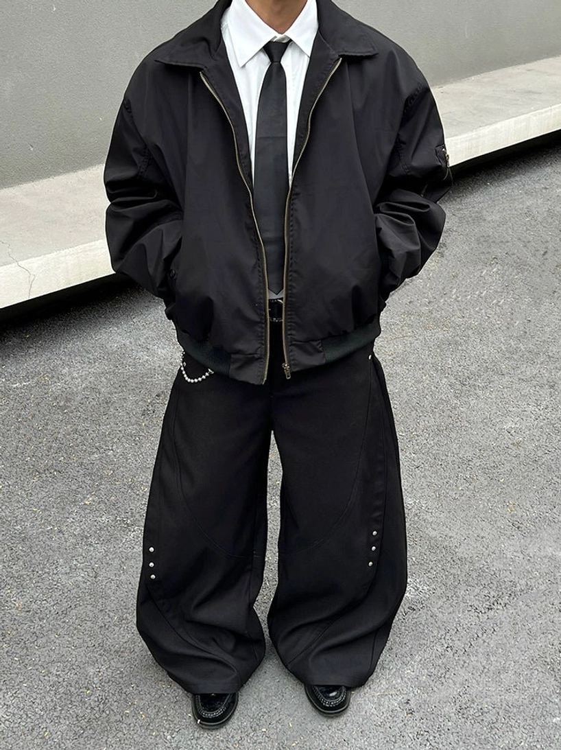 Full-length streetwear outfit featuring a white oversized dress shirt, black bomber jacket, dark tie, wide-leg trousers, chain belt, and polished leather shoes