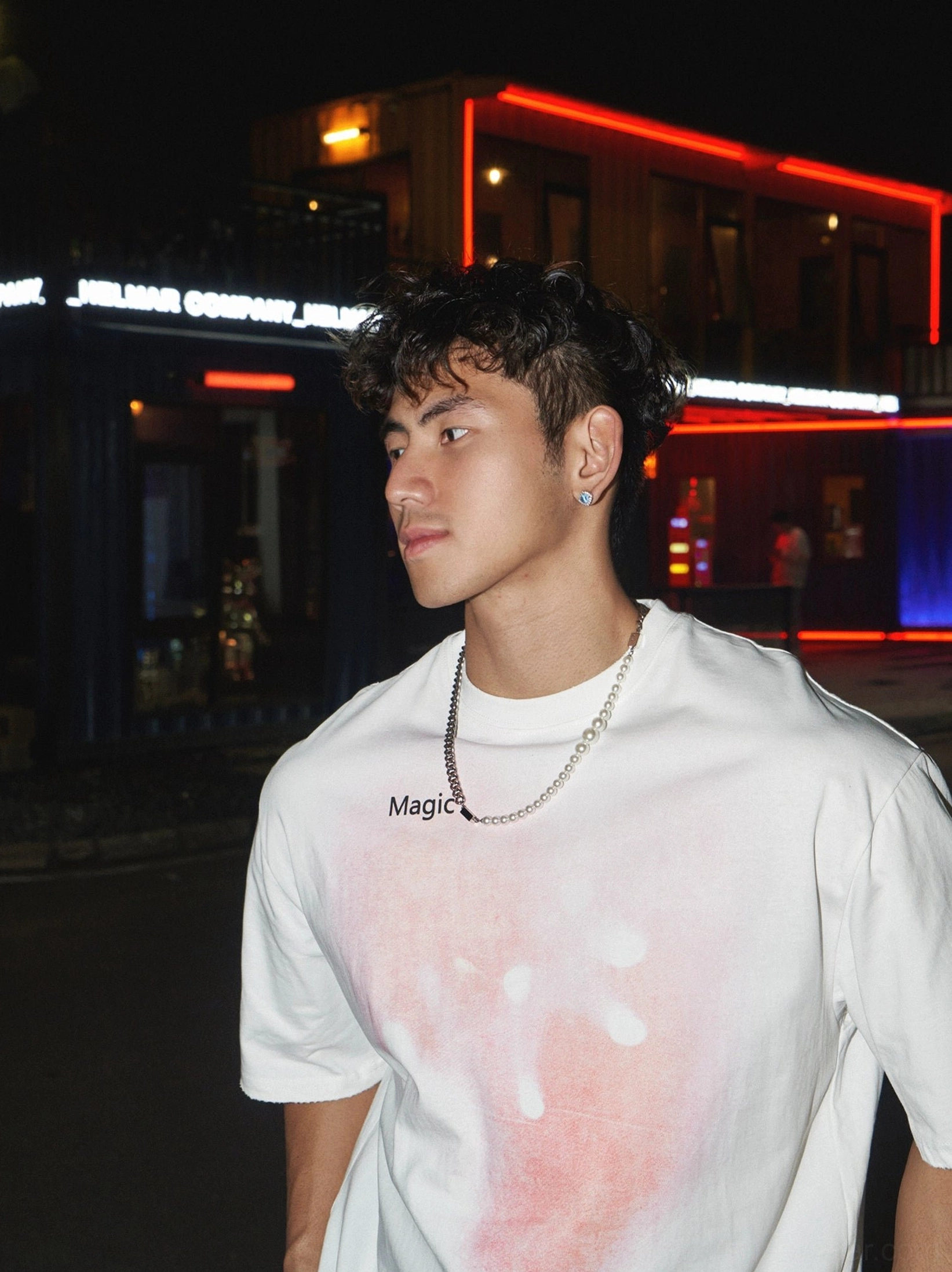 White oversized streetwear T-shirt with pink gradient splatter graphic and Magic chest logo styled in a neon Seoul-inspired night street