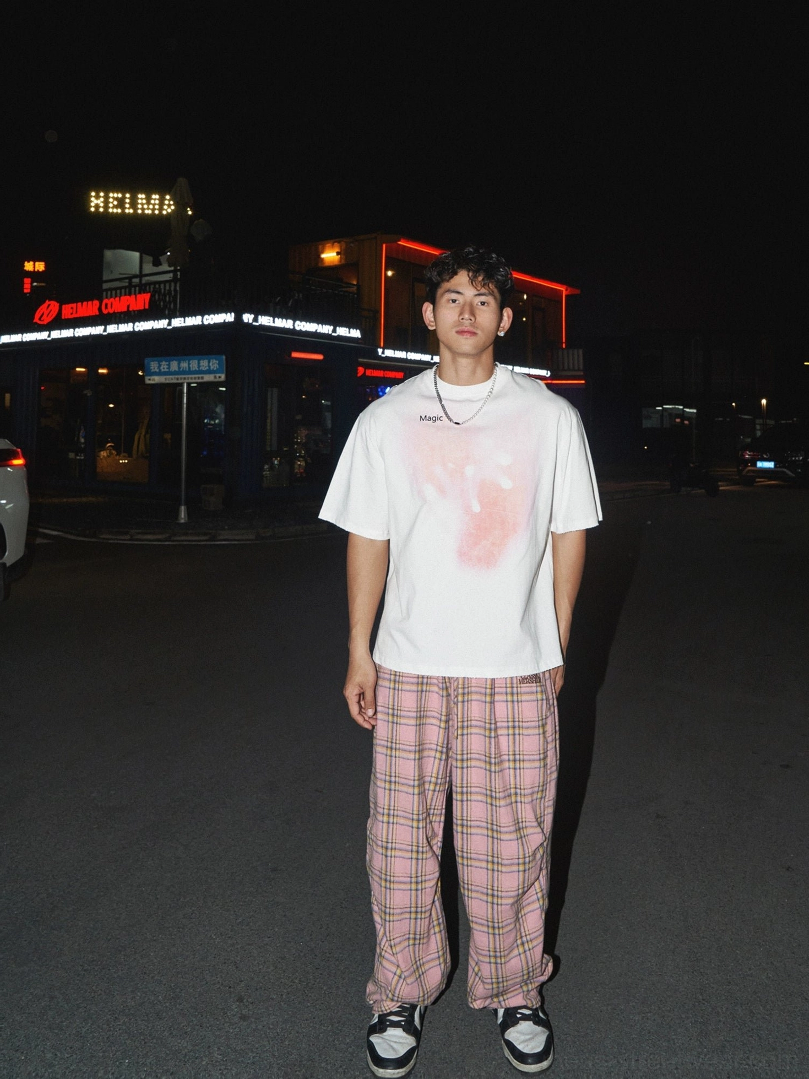 Full-body view of a white oversized pink gradient splatter T-shirt styled with pink plaid trousers and skate shoes