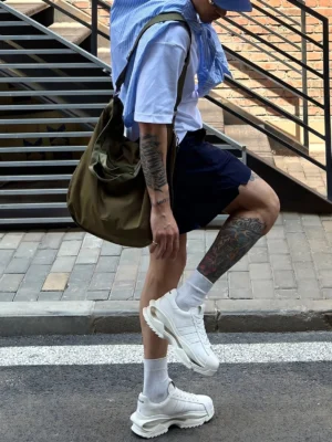 White unisex platform sneakers worn by a tattooed male model on an urban stairway in a contemporary Seoul streetwear outfit
