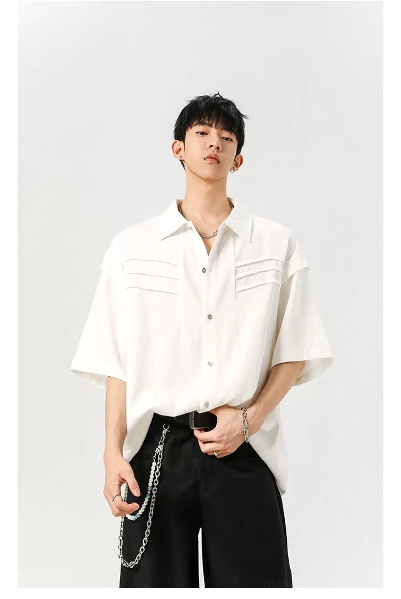 White oversized pleated panel shirt styled with wide-leg black trousers and layered silver chain accessories