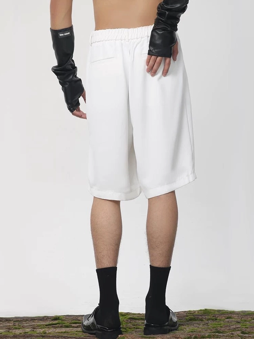 White pleated tailored longline Bermuda shorts shown from the rear with a relaxed wide-leg silhouette, smooth suiting fabric, and modern Korean streetwear styling