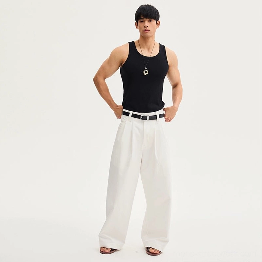 Full-body front view of white pleated wide-leg trousers styled with a black tank top, black leather belt, and leather slides