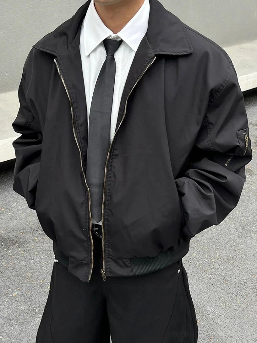 Close-up of a crisp white pointed collar dress shirt and dark tie layered beneath an oversized black zip bomber jacket