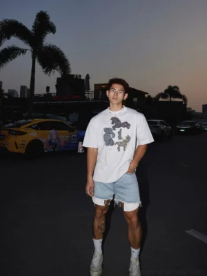 Full body Asian male model wearing white pony animal graphic cotton T-shirt with frayed denim shorts socks and sneakers at dusk