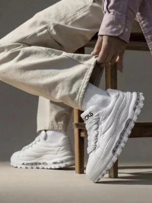 White leather trail runner sneakers worn with beige trousers and light purple top in a casual streetwear outfit