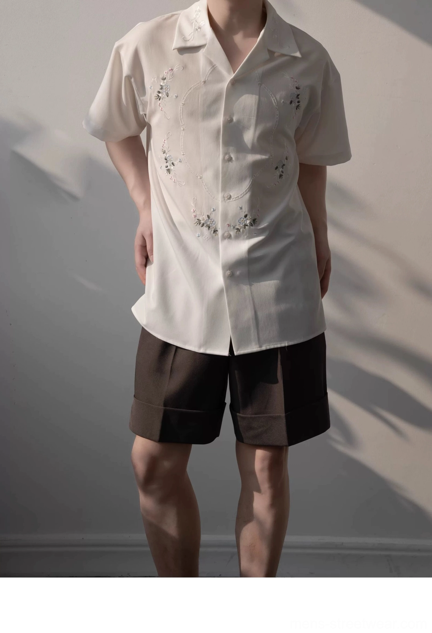 Male model wearing a relaxed white embroidered camp shirt with subtle floral motifs and brown suit shorts