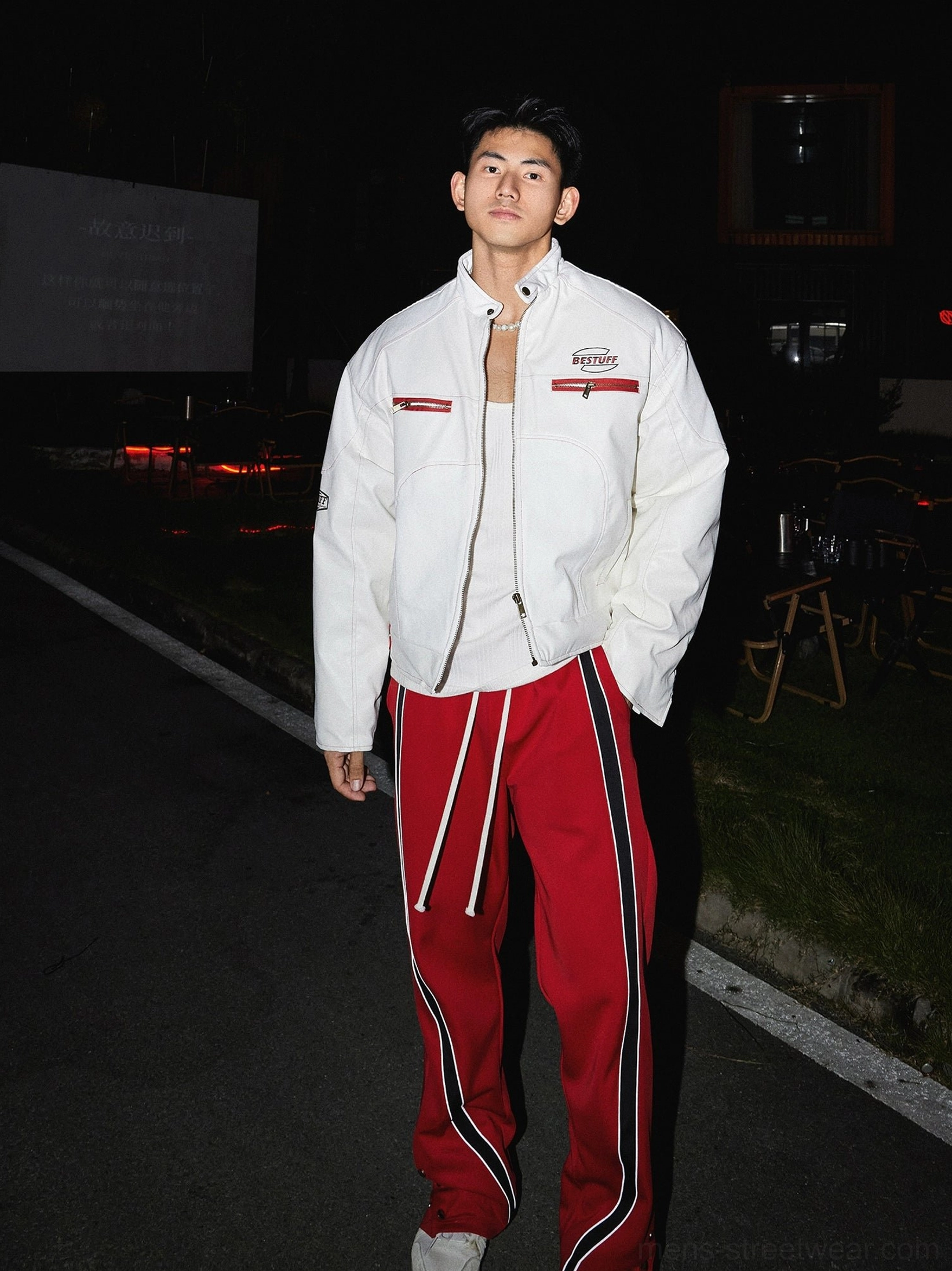 White retro racing winter streetwear jacket back three-quarter view styled with red striped track pants at night