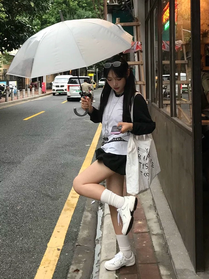 White casual retro runner sneakers styled with a mini skirt, knee-high socks, and layered streetwear on a downtown roadside