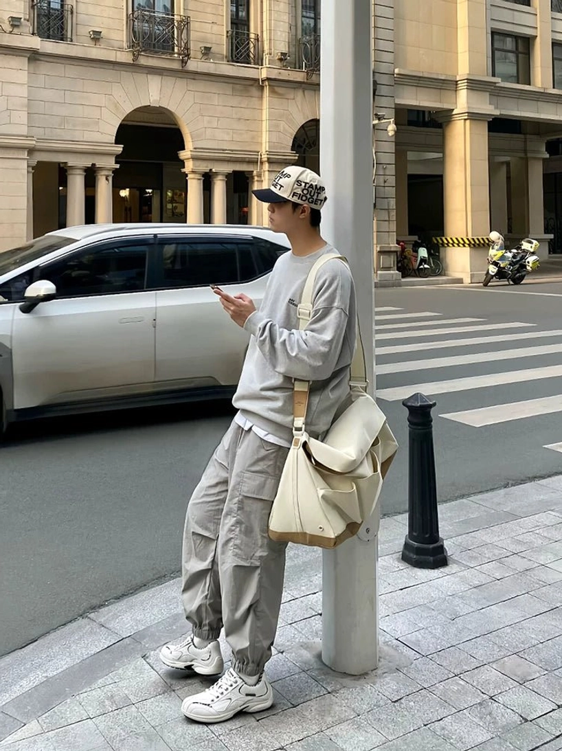 White retro running sneakers worn with layered casual clothing, a printed cap, and crossbody bag at an urban crosswalk