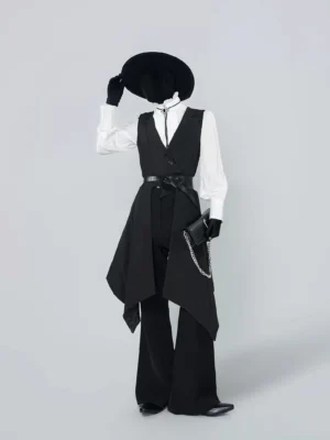 Three quarter view of a white ruffled stand collar blouse layered with an asymmetric black waistcoat, wide leg trousers, detachable skirt, belt, and chain handbag