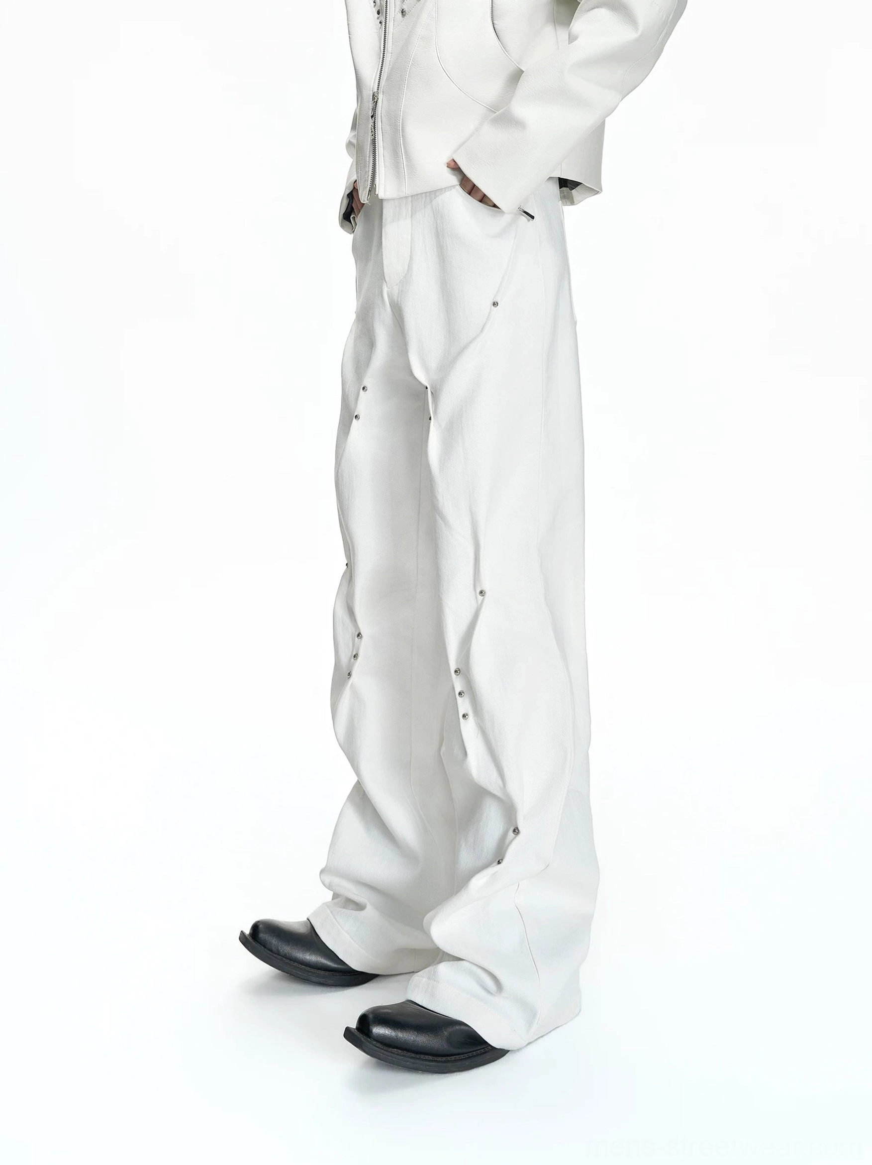 Side view of white sculptural flared denim pants showing metal rivets curved seam construction and long hem