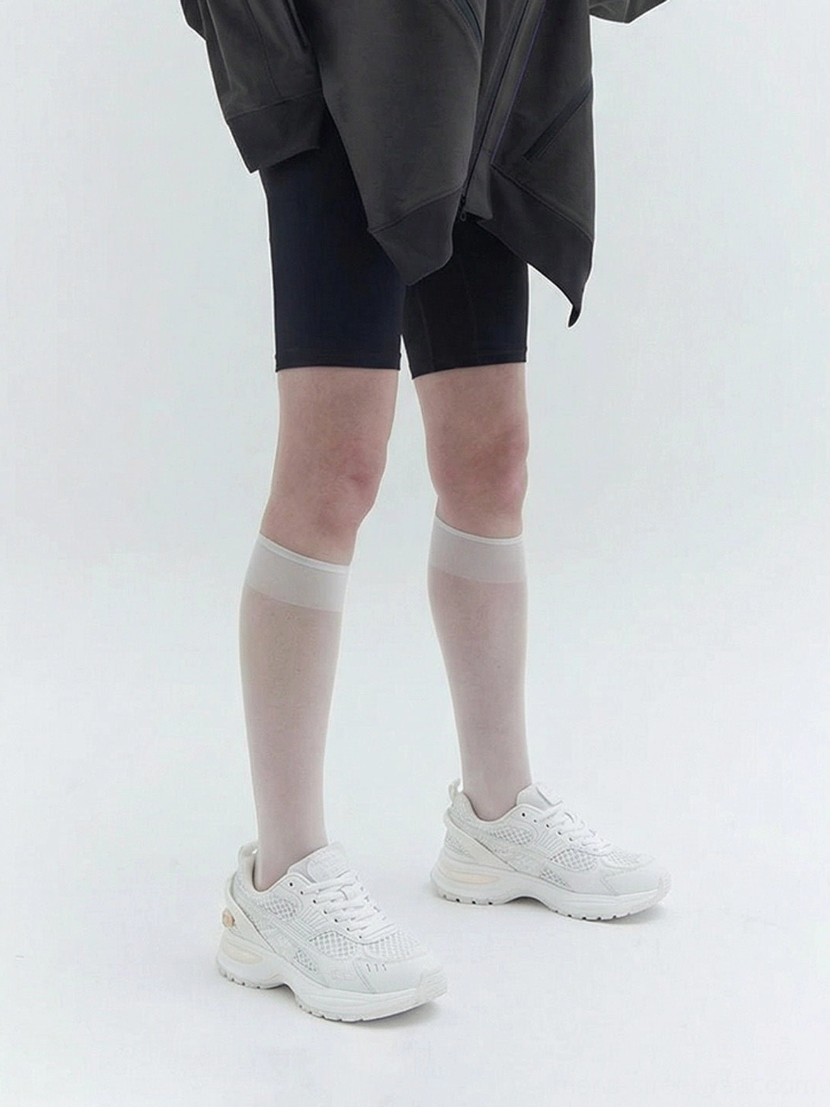 White sculpted-sole running sneakers styled with black biker shorts and sheer knee-high socks for a modern streetwear look