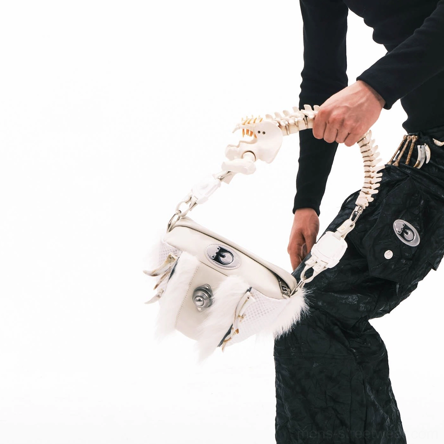 White sheepskin leather fur bag with sculptural faux bone spine handle held by model wearing black cargo pants