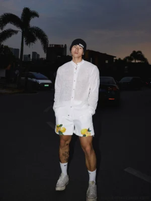 Full body view of a white lightweight sheer woven shirt styled with printed shorts and sneakers in Seoul inspired streetwear