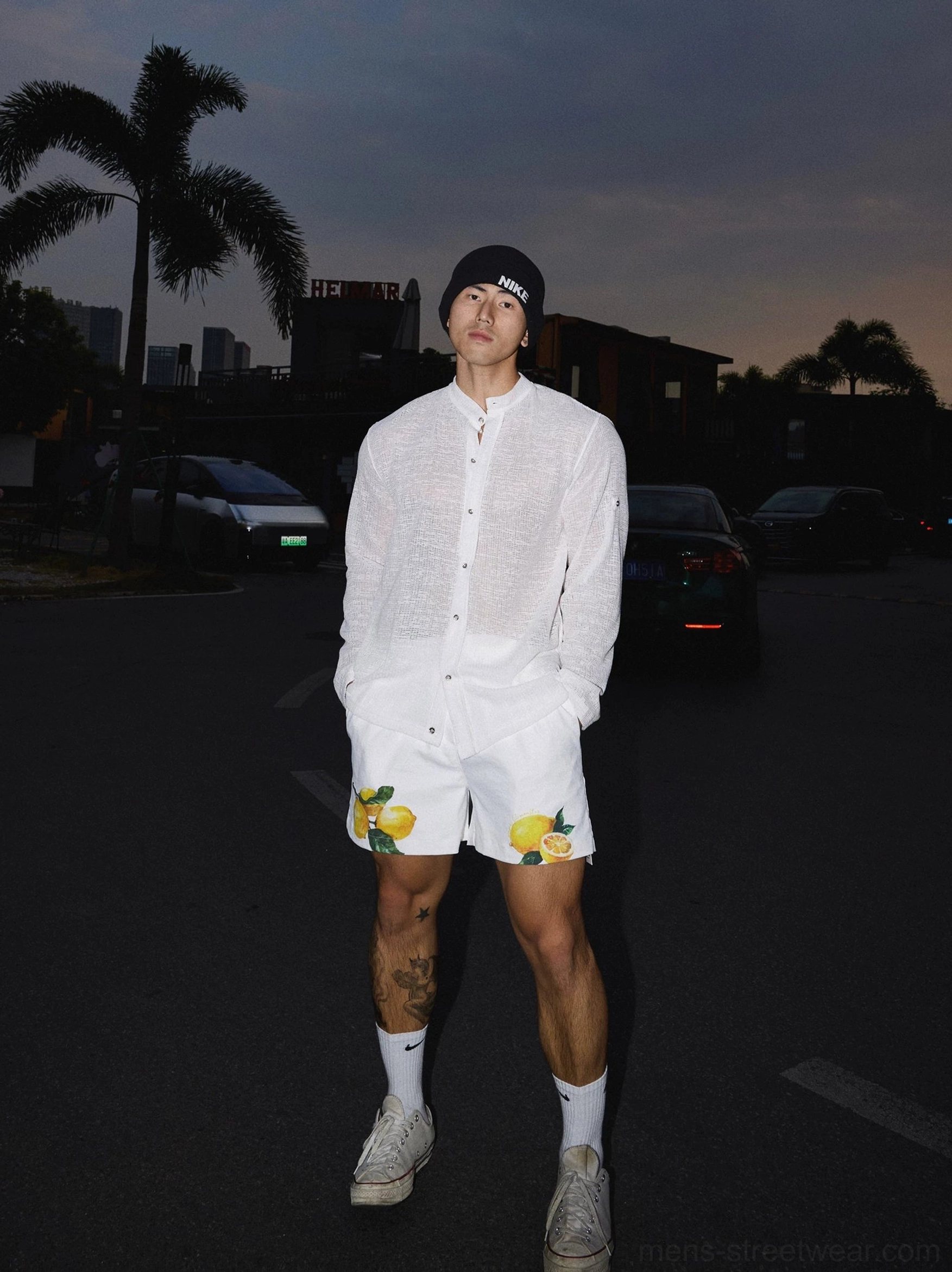 Full body view of a white lightweight sheer woven shirt styled with printed shorts and sneakers in Seoul inspired streetwear