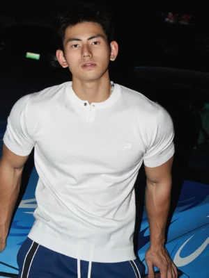 White minimalist single-button Henley knit streetwear T-shirt worn by male model beside a blue car