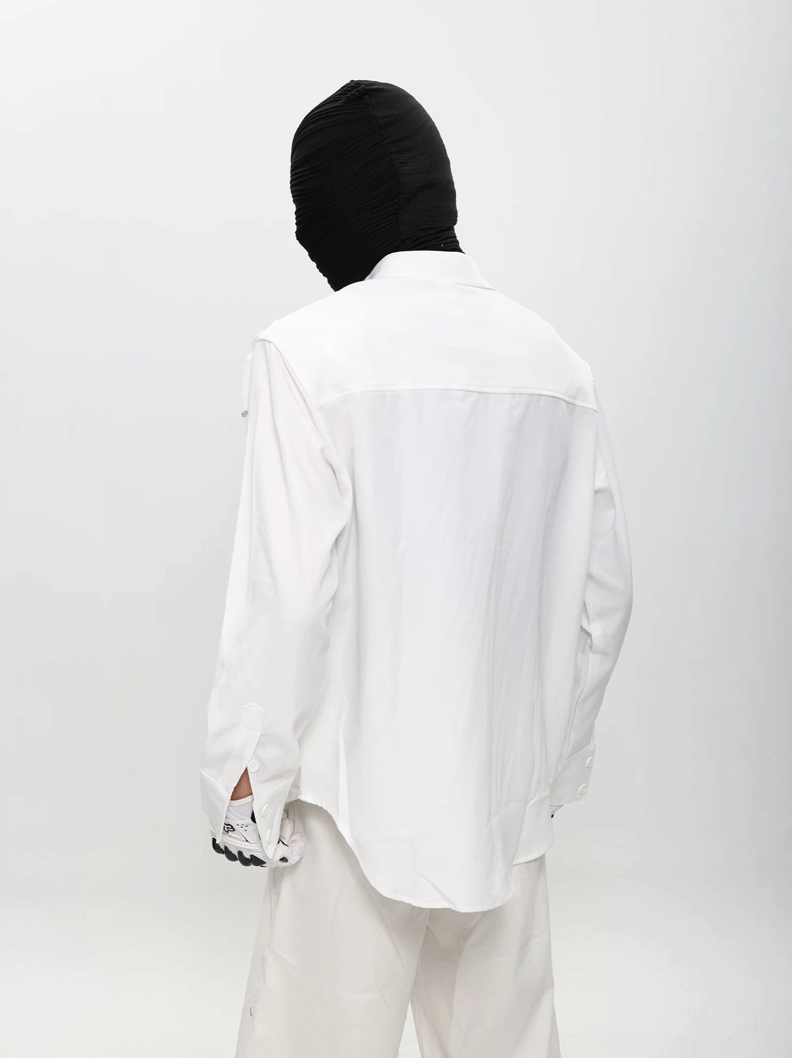 Back view of white relaxed fit button up shirt with subtle speckled print, curved hem, and long sleeves styled in monochrome streetwear
