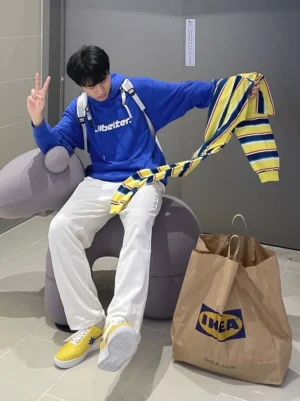 White straight-leg denim jeans paired with a blue graphic hoodie and yellow blue striped knit layer for Korean casual streetwear