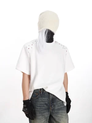 White studded shoulder boxy streetwear T-shirt shown from a front three-quarter view with relaxed fit, crew neck, wide sleeves, and Seoul-inspired styling