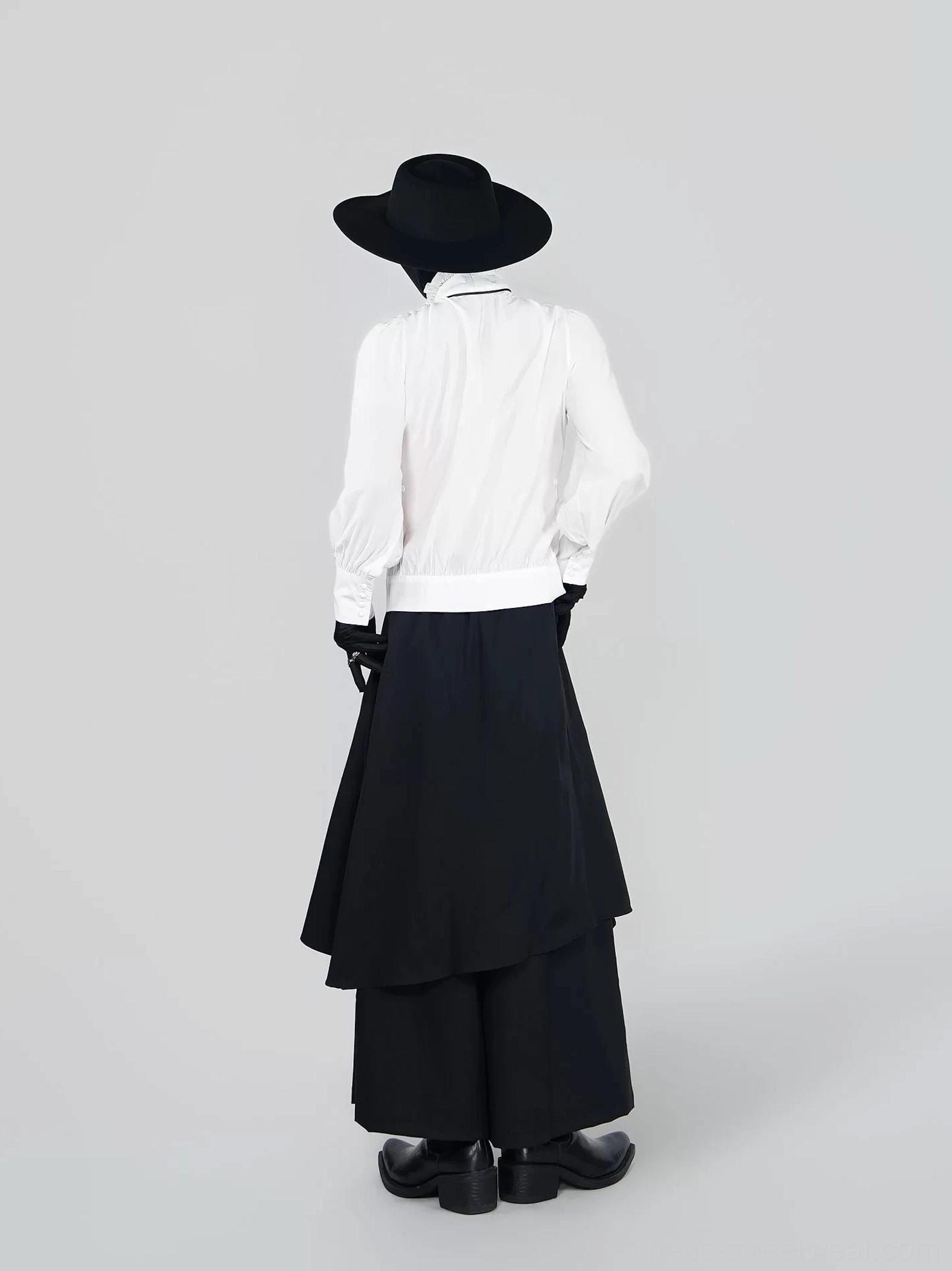 Back view of a white tailored ruffle blouse with long sleeves styled with a black layered asymmetric wide leg skirt and dark gothic accessories