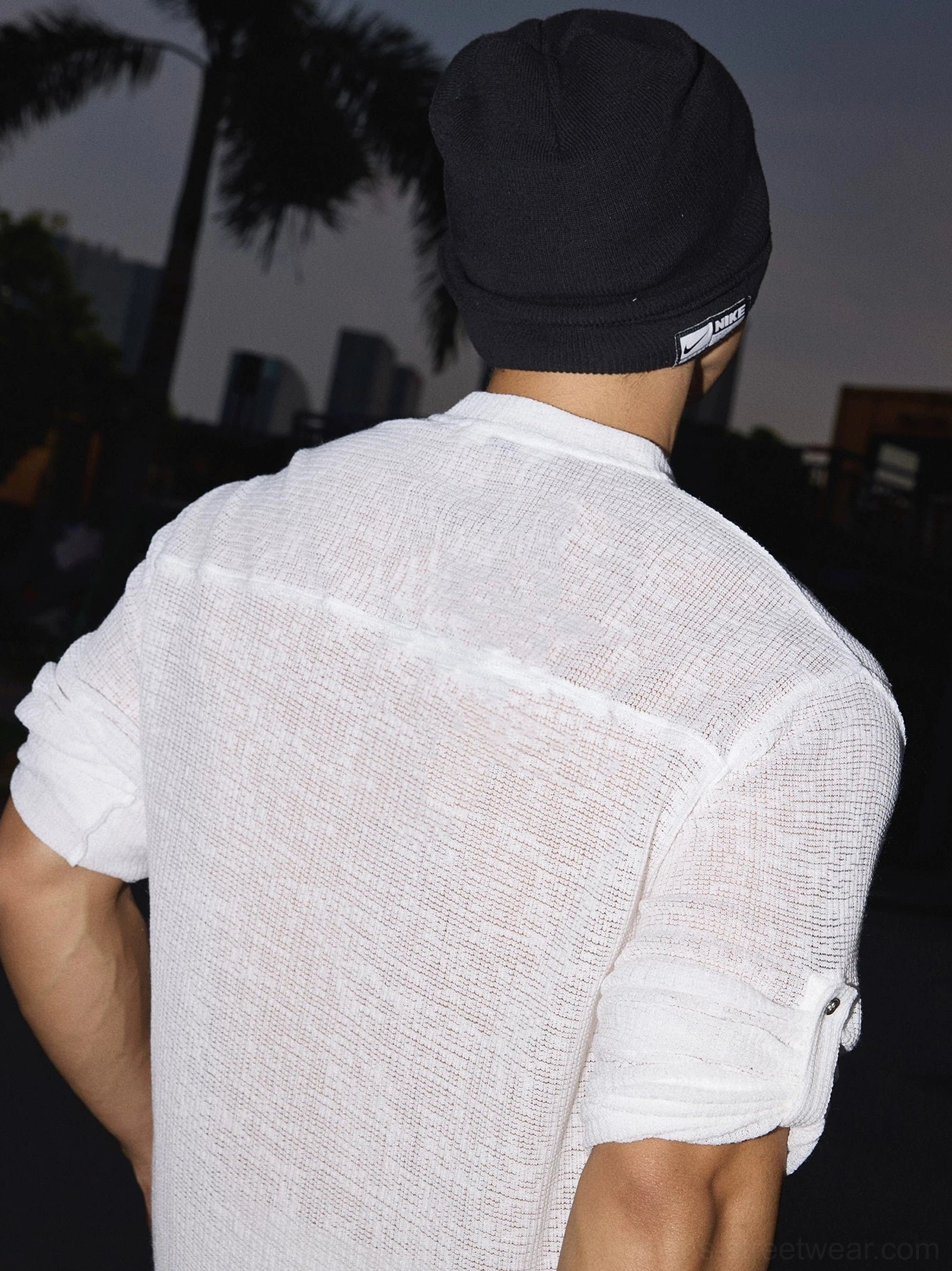 Back view of a white textured stand collar shirt showing relaxed drape, back seam, and buttoned sleeve cuffs